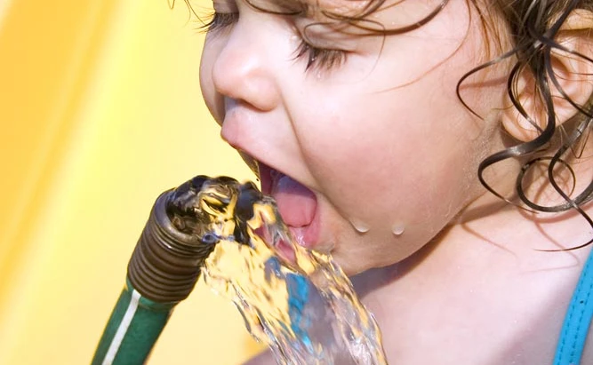 A young girl drinks water from a hose