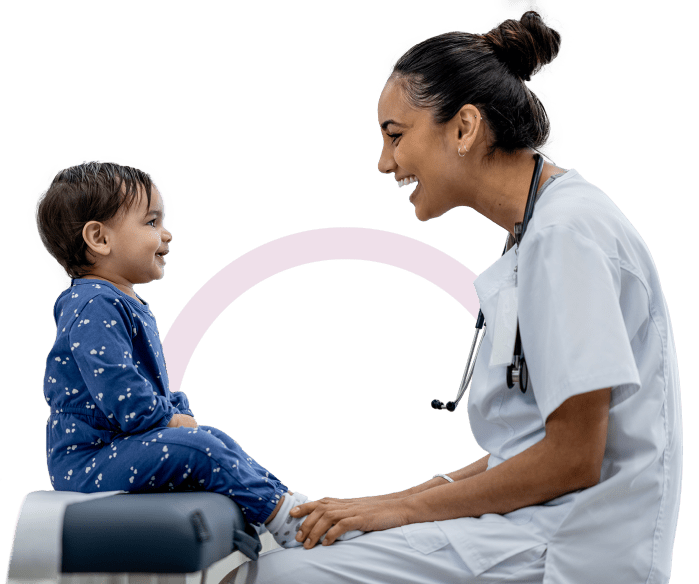 Female doctor smiling and looking at a smiling infant that is sitting on an examination table